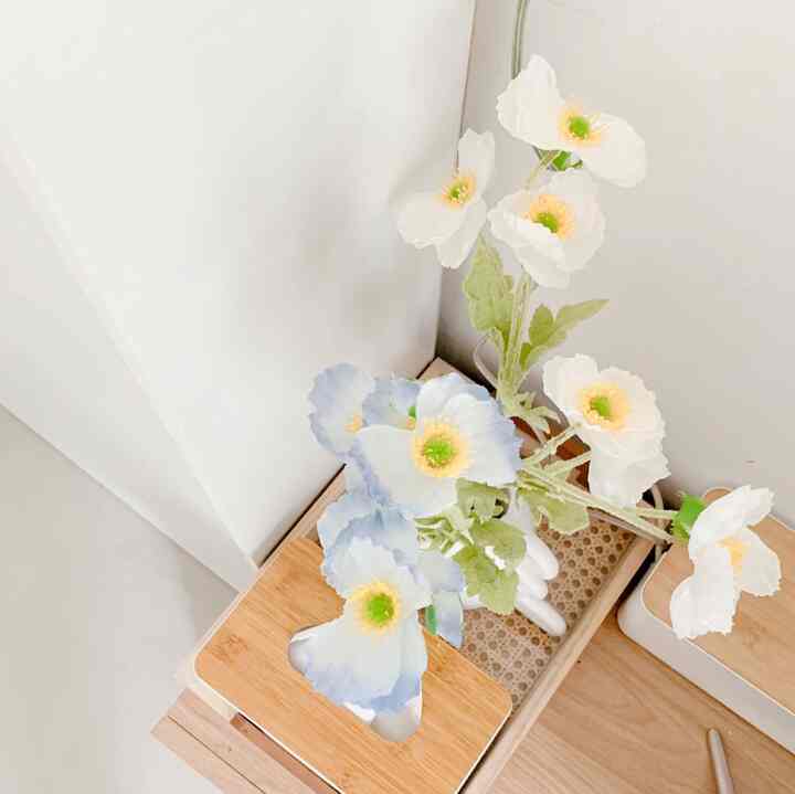 A minimalistic space featuring white walls and wood-tone table with white and pale blue flowers arranged