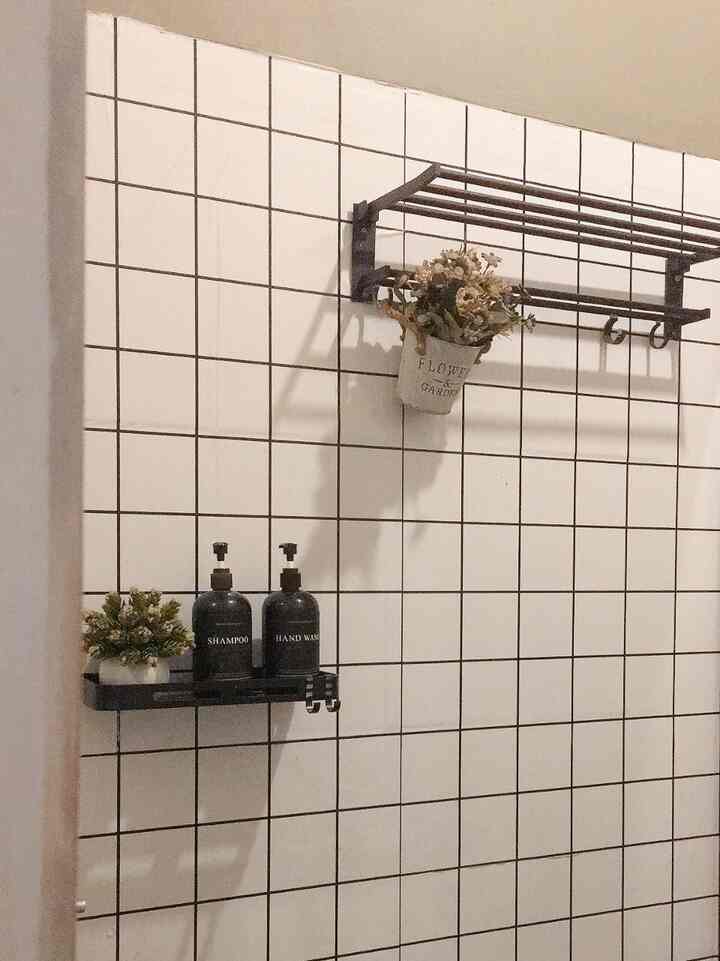 Bathroom space with white tiled walls, black shelves holding shampoo bottles and flower decorations