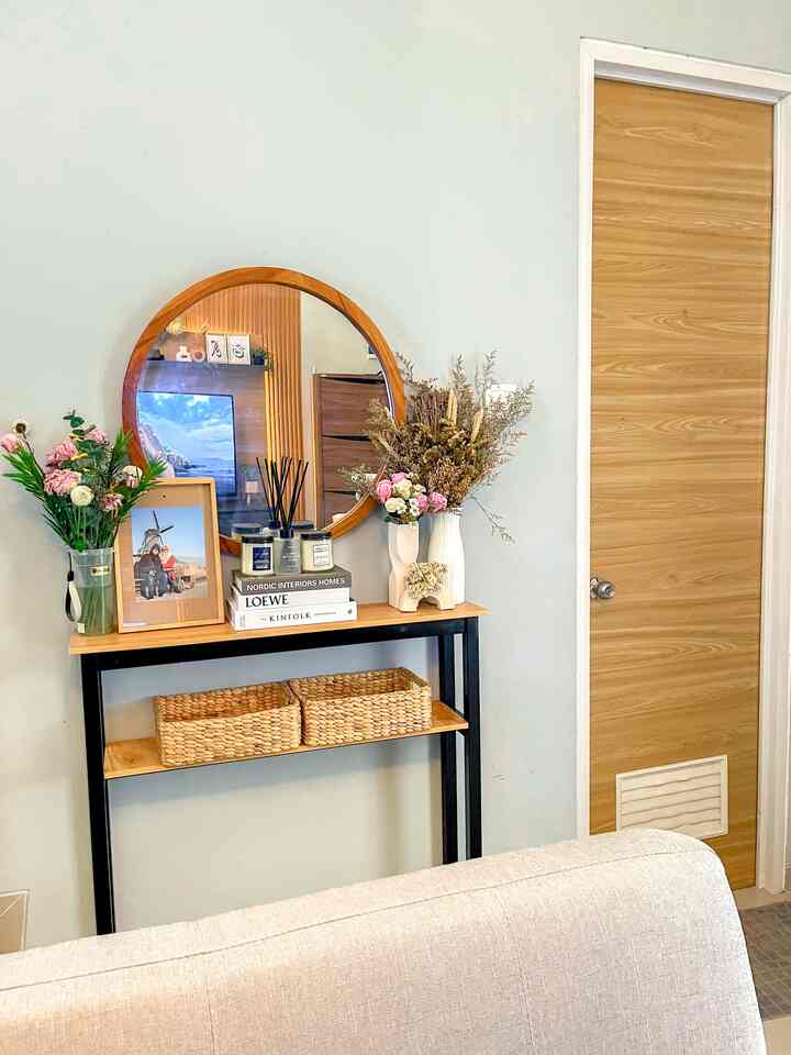 Beige and wood-toned living room entrance featuring a round mirror, console table with vases and picture frames, creating a cozy atmosphere