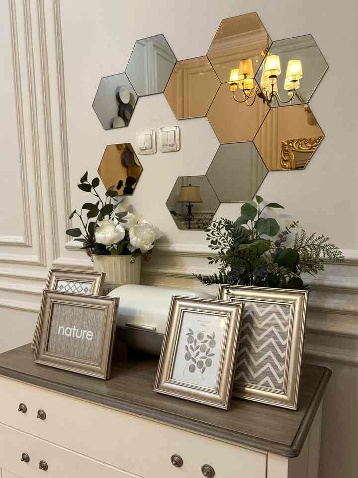 A gold and beige toned living room wall featuring hexagonal mirrors, plants, and gold picture frames creating a luxurious interior