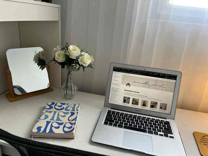 White-toned home office featuring a laptop, notebook, and vase creating a clean and quiet workspace