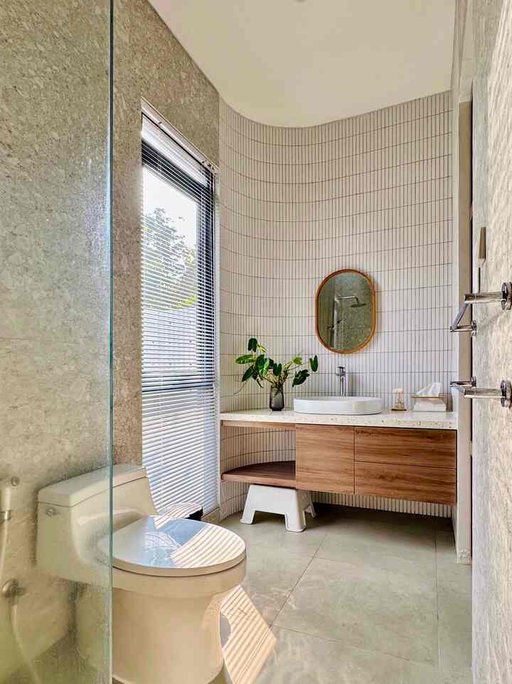 A compact bathroom with harmonious white and wood tones, morning sunlight streaming through window blinds brightening the space