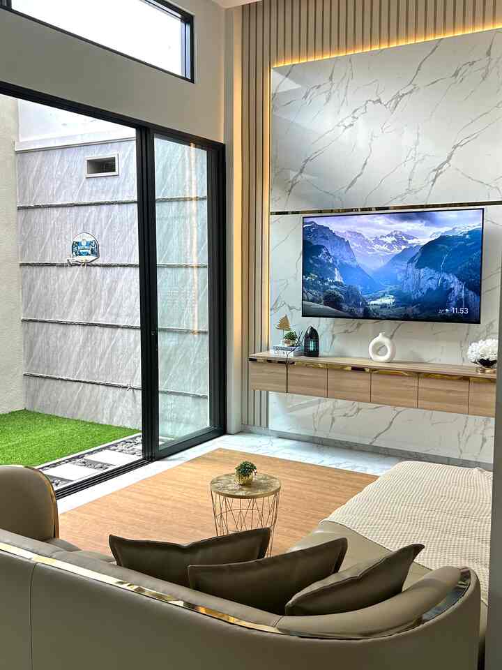 A modern living room with natural wood tones and white hues, featuring a sofa and wall-mounted TV in a clean and bright interior