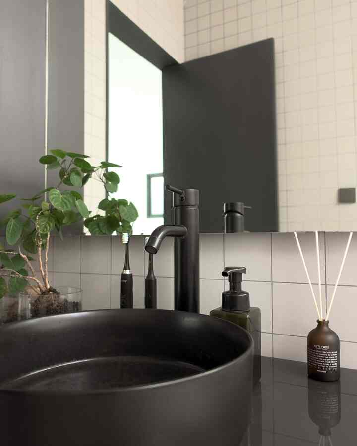Matte black bathroom washbasin with faucet, diffuser, and mirror arranged in a simple modern space