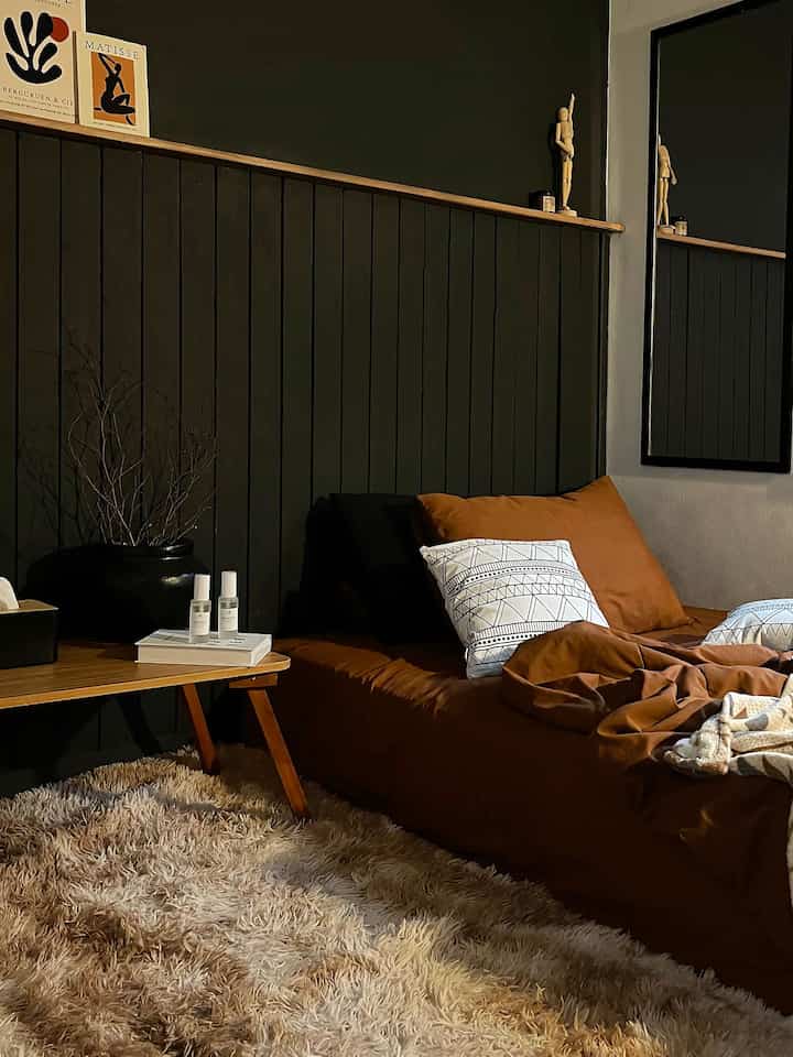 A cozy bedroom in brown and black tones featuring comfortable bedding and a wooden side table with warm ambiance