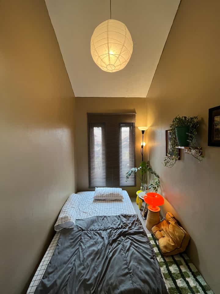 Warm brown compact bedroom featuring bed, gray blinds, plants, and ambient lighting in a minimalist design