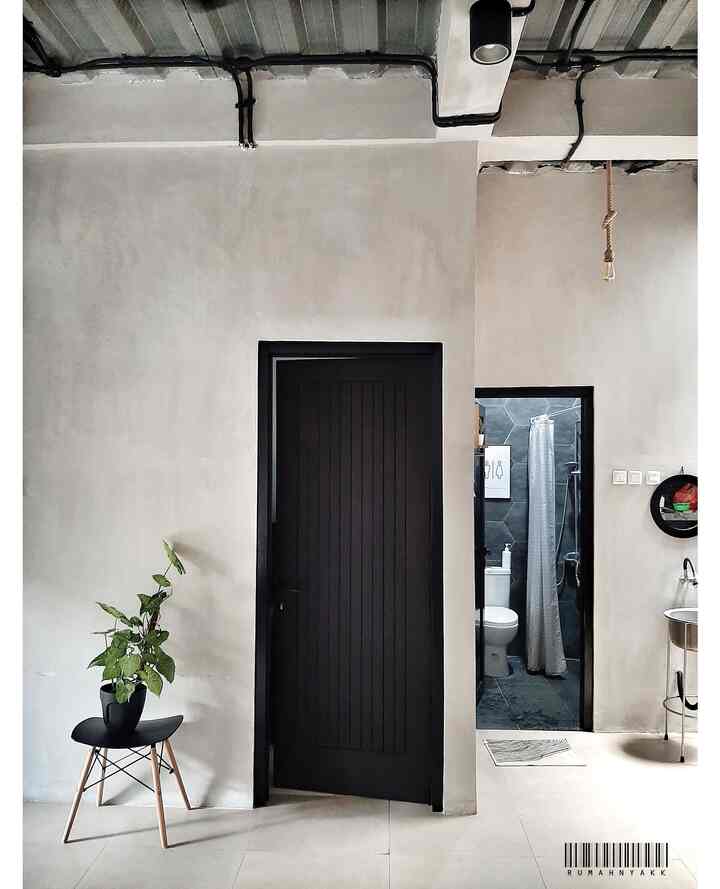 White and black industrial-style space featuring a bathroom entrance and a plant on a minimalist chair
