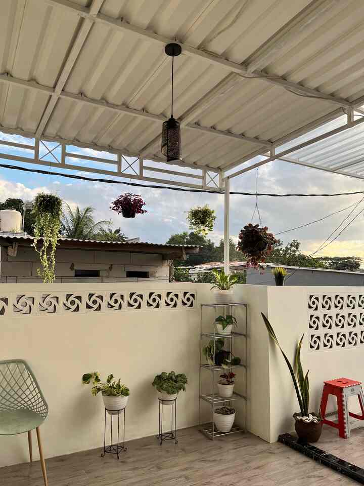 Beige-walled balcony with wood-tone floor featuring various potted plants and a stool creating a natural relaxation space