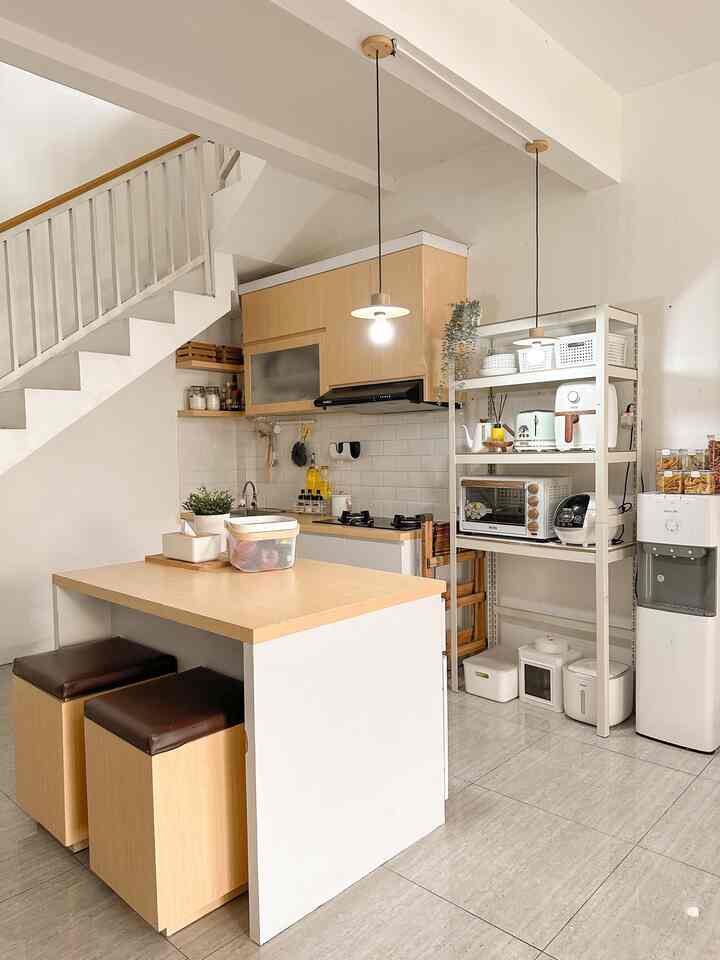 A compact kitchen space with white and wood tones, featuring cooking utensils and pendant lighting