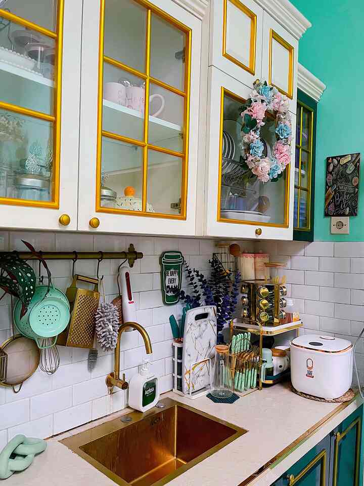 Mint and gold accented kitchen space featuring a gold sink and white tiled walls with neatly organized kitchen utensils creating a cozy atmosphere