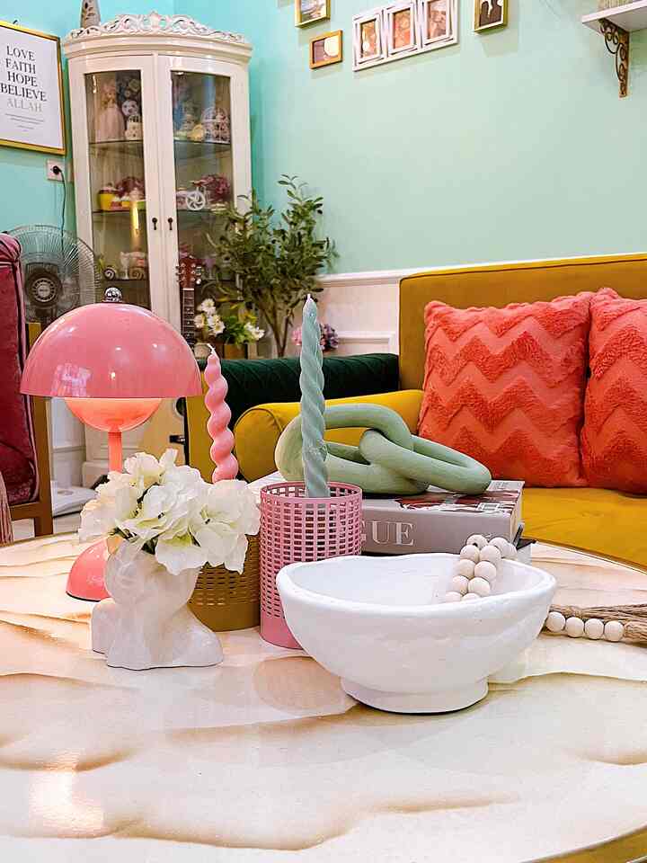 Bright yellow sofa with pink cushions in living room, marble coffee table topped with various objets and candles in a simple natural setting