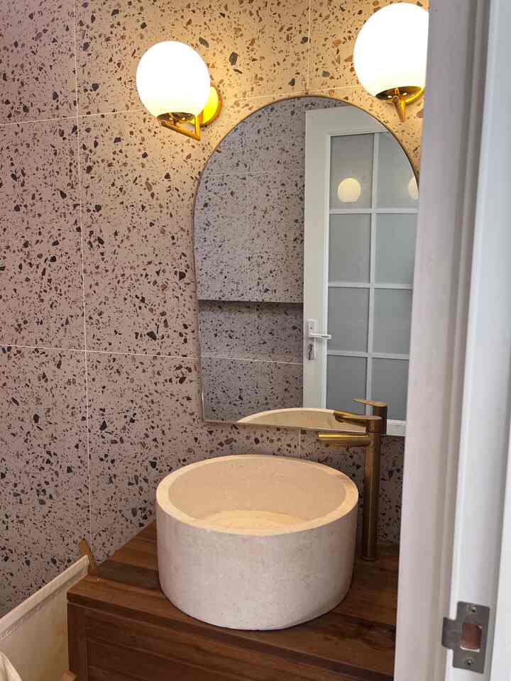 Natural wood tone bathroom wash area with terrazzo walls and gold faucet accents
