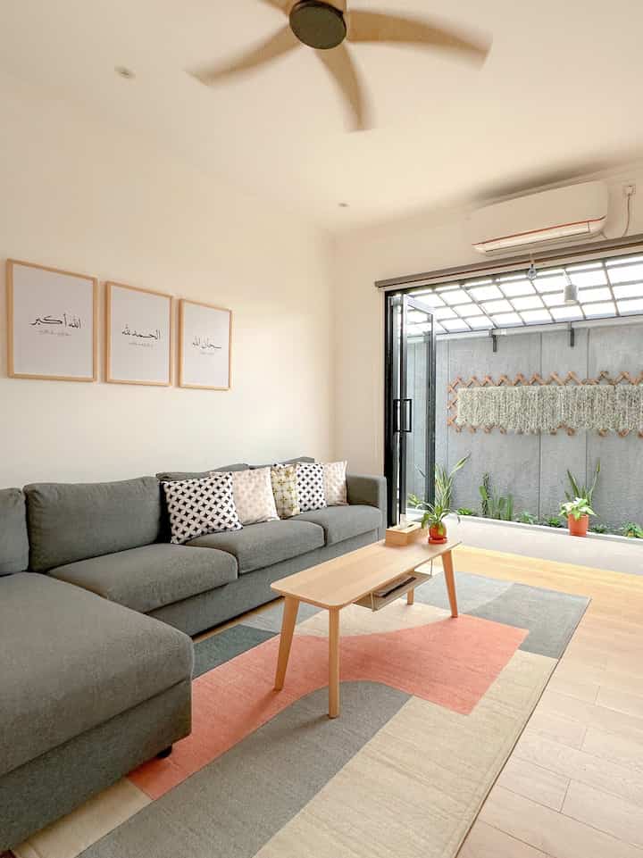 Natural-toned living room featuring a dark gray sofa, wooden coffee table, and visible balcony with plants, creating a cozy atmosphere