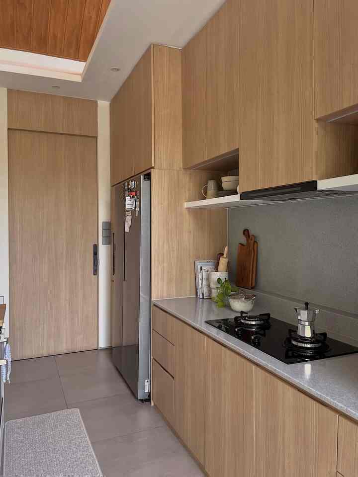 Compact modern kitchen with natural wood tone built-in cabinetry, featuring a gas stove and refrigerator