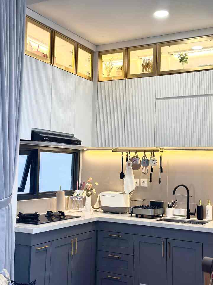 Modern kitchen in white and navy tones featuring upper and lower cabinets, countertop appliances, and hanging kitchen utensils