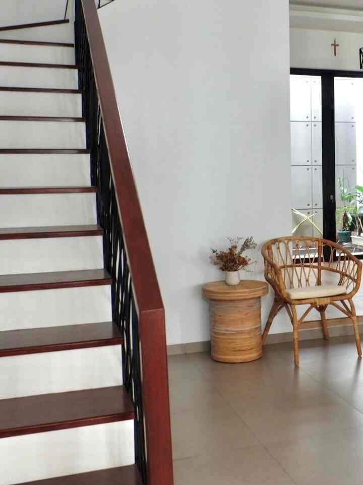 Natural wood-tone stairs with a rattan chair and side table furnishing a cozy entrance area
