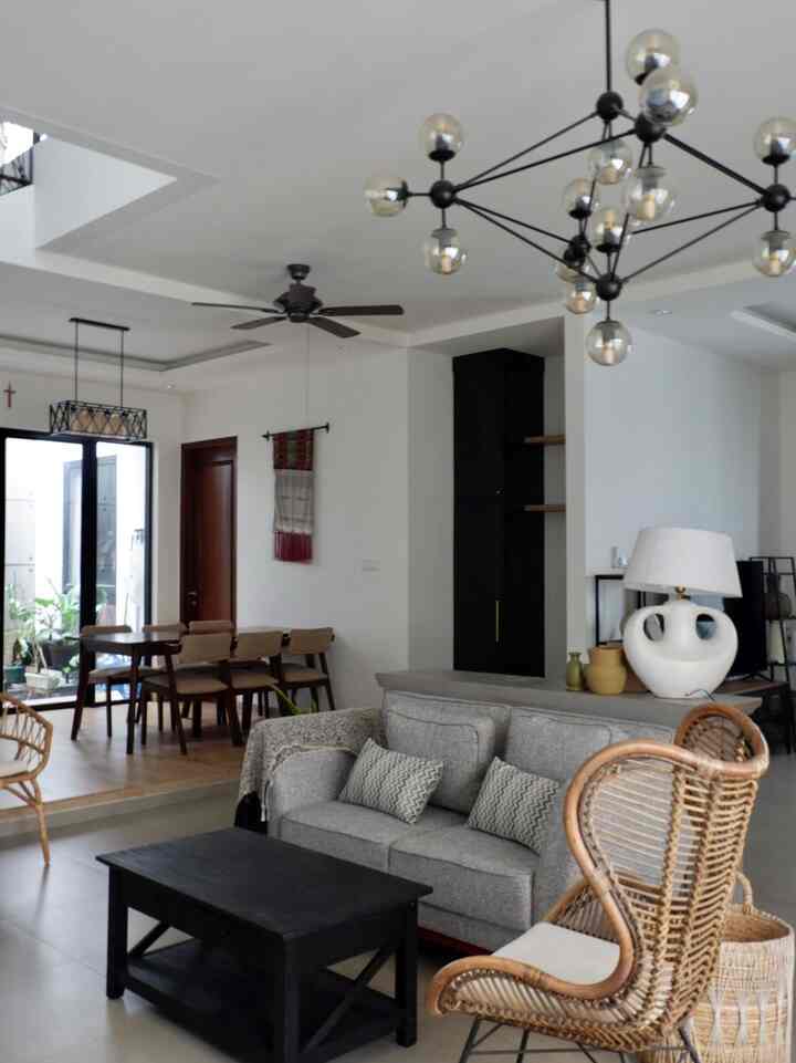 White and gray toned living and dining room featuring a gray sofa, rattan armchair, black coffee table, and distinctive modern lighting