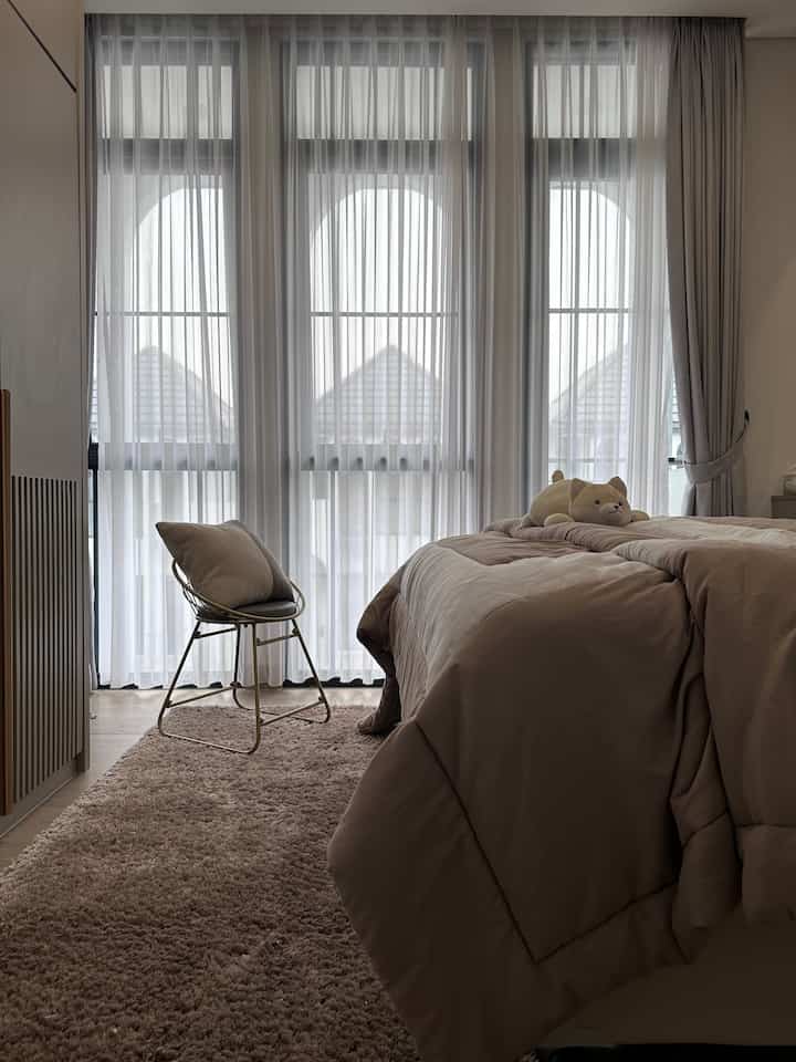 Beige-toned bedroom with bed featuring pillows and a metal chair, creating a cozy and tidy space