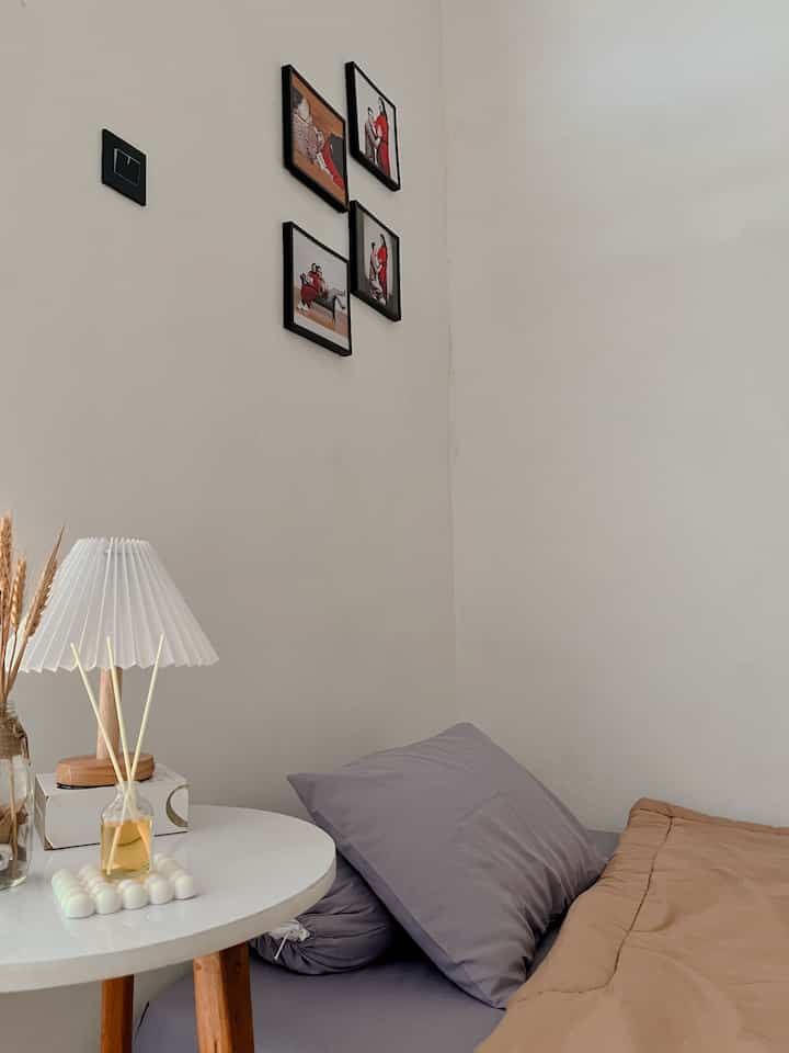 Simple natural bedroom with white walls, beige bedding, and round wooden-legged table