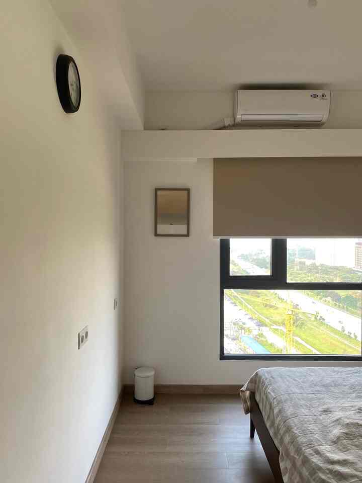 White and natural color bedroom featuring a large window with beige curtain and wooden flooring, creating a clean and cozy atmosphere