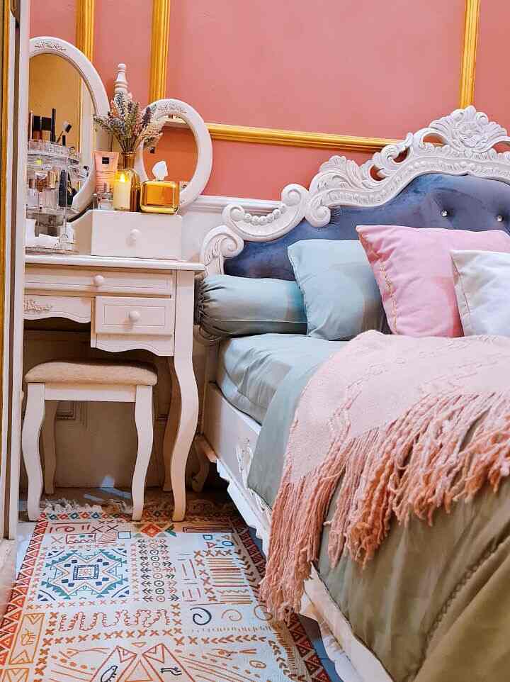 A vintage-style bedroom with pink walls and a Bohemian rug, featuring a vanity and decorative items creating a feminine atmosphere