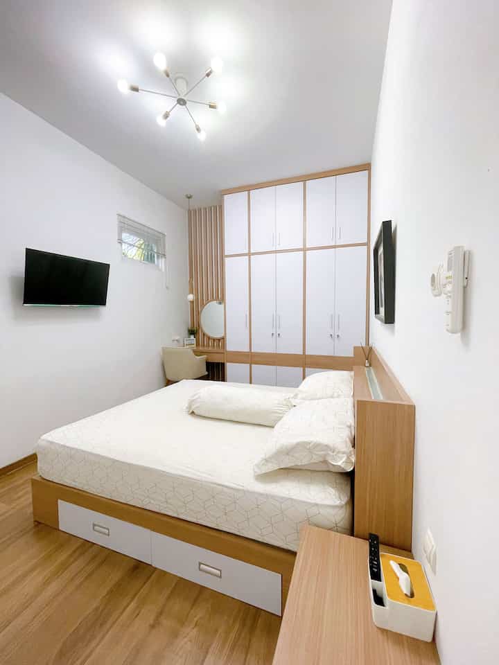 Bright bedroom with white and wood tones featuring a large built-in closet and custom bed frame in a simple setting
