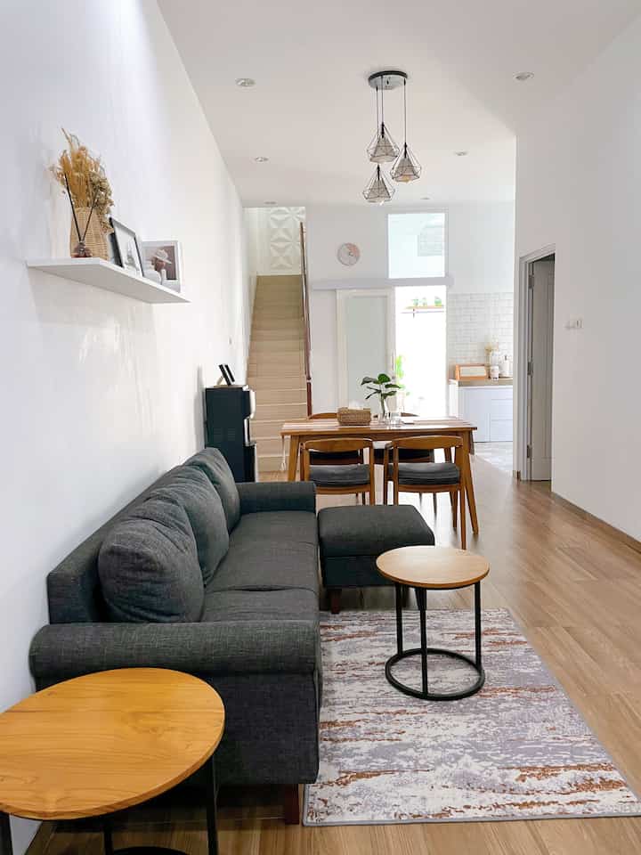 Modern living and dining room with white walls and ceiling, gray sofa, and natural wood-toned dining set creating a harmonious space
