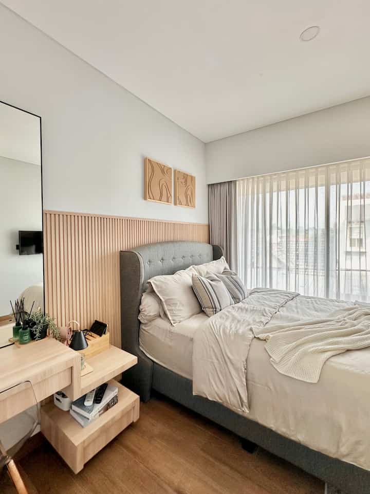 Bright bedroom with white and wood tones, featuring a gray bed and sheer curtains for a natural ambiance