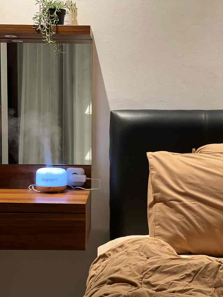 Cozy bedroom with brown bedding and wood-tone nightstand, featuring a diffuser emitting soft light and mist