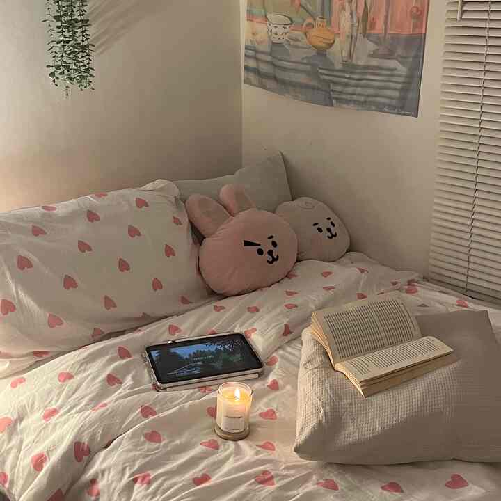 Warm beige and pink toned bedroom featuring heart-patterned bedding, character pillows, and a lit candle creating a cozy atmosphere