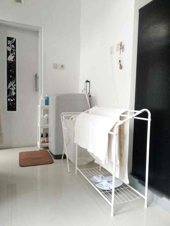 Clean white and gray toned small laundry space featuring a washing machine, drying rack, and floor mat with practical arrangement