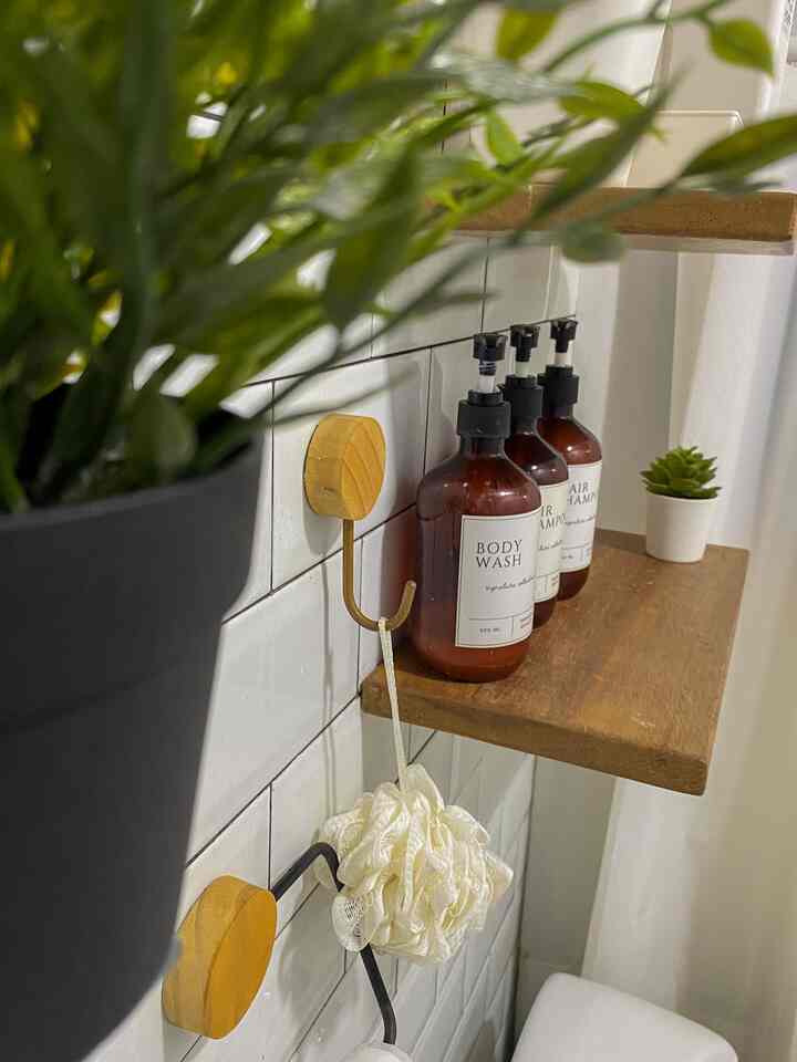 Cozy bathroom corner with white tiled walls, wood-tone shelf, wooden hooks holding bath essentials