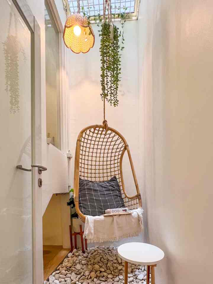 Natural color and wood tone small living room corner featuring rattan hanging chair and white round side table creating a cozy atmosphere.