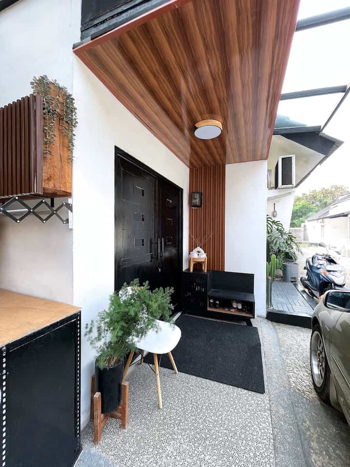 Black and brown toned entrance featuring wooden ceiling and PVC wall panels creating a warm, bold exterior façade