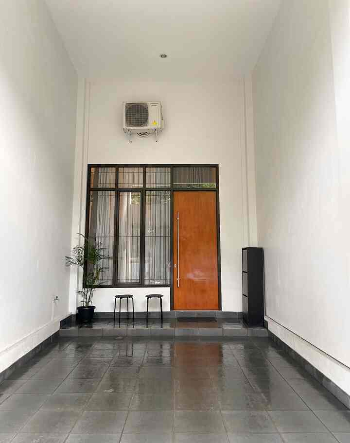 Minimal carport and veranda space with white walls and khaki wooden door, featuring black stools and a cabinet