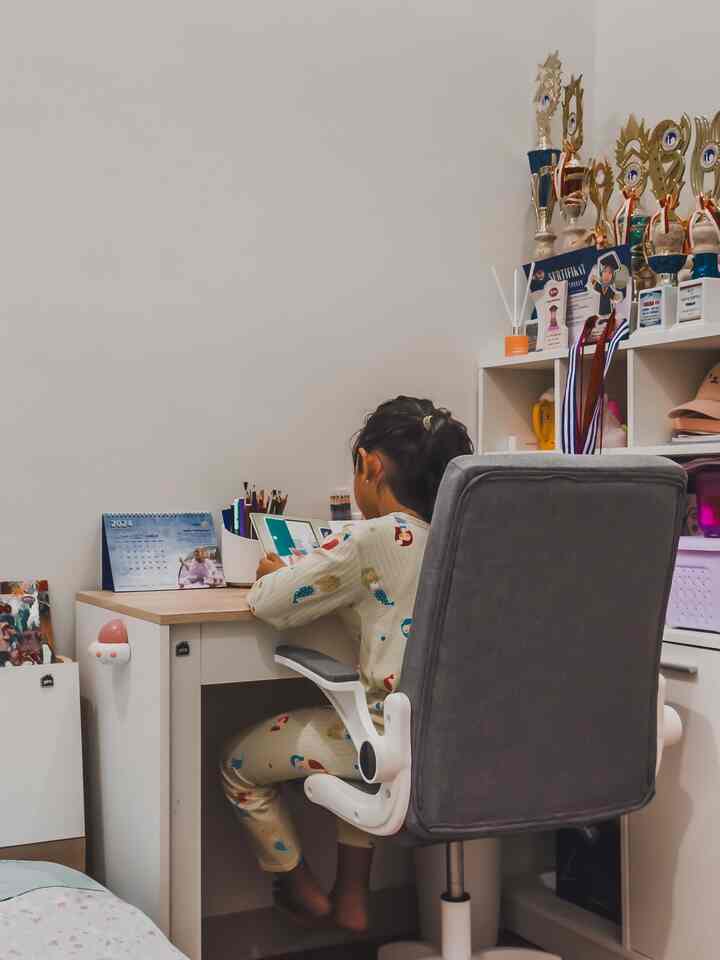 A compact kids' room in white and wood tones featuring a child studying at a desk with a cozy atmosphere