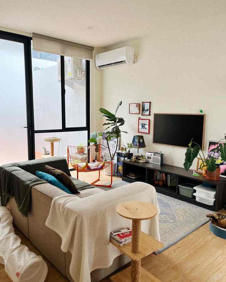 Natural-tone mid-century modern living room featuring beige sofa, orange armchair, and cat tower creating a cozy atmosphere