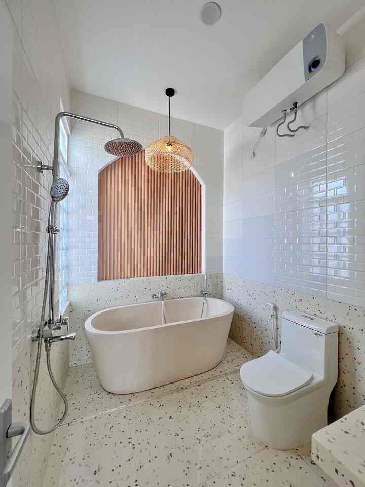 Minimal bathroom with white tiles and brown arch wall panel, featuring a central bathtub and rain shower creating a soothing ambiance