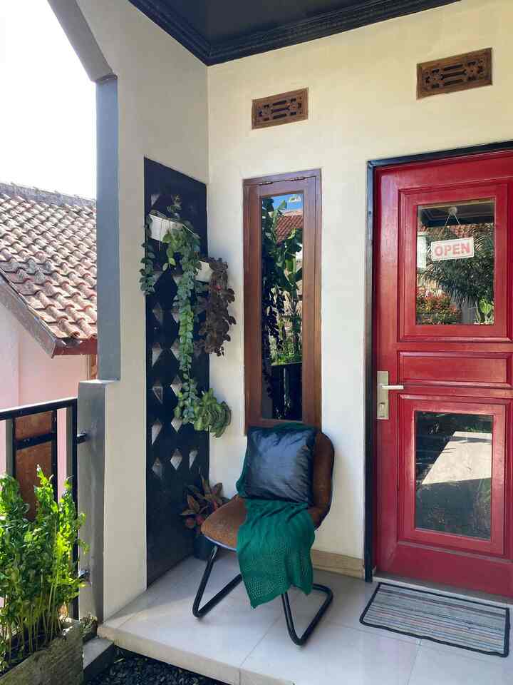 White walls and floor entrance featuring a red door, brown armchair with green throw, and hanging plants creating a cozy atmosphere