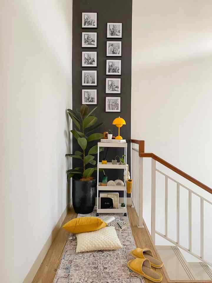 Charcoal and white toned narrow corner by stairs featuring plant, storage rack, and cushions creating cozy relaxation space