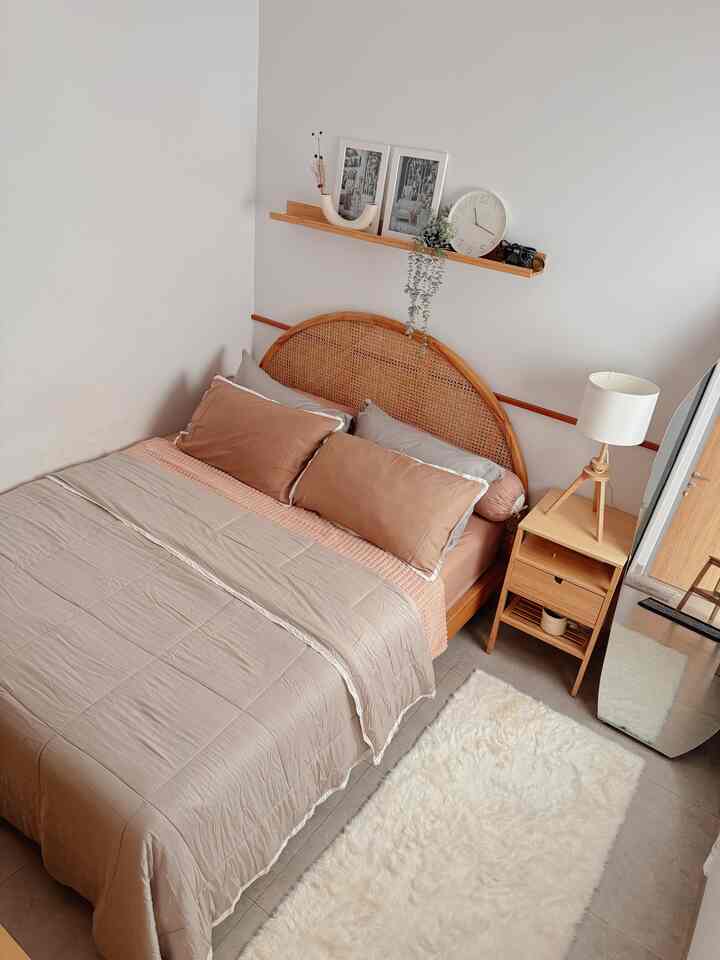 Natural-toned compact bedroom featuring arc-shaped rattan bed, abstract mirror, Scandinavian style lamp, and white rug creating cozy atmosphere