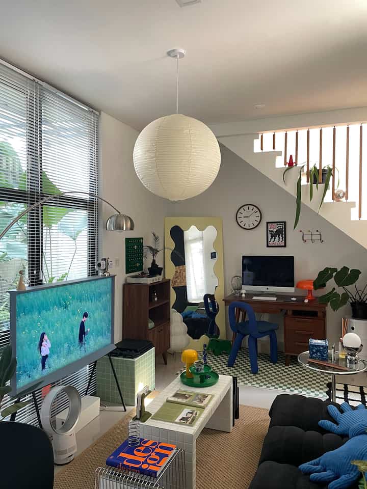 White and black toned mid-century modern living room featuring sofa, pendant light, desk, and wavy mirror in a cozy atmosphere