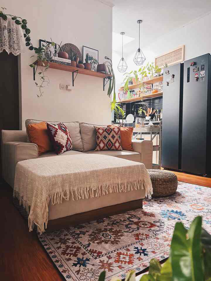 Beige and brown toned living room featuring a beige sofa, colorful patterned carpet, wooden shelves with plants creating a natural interior