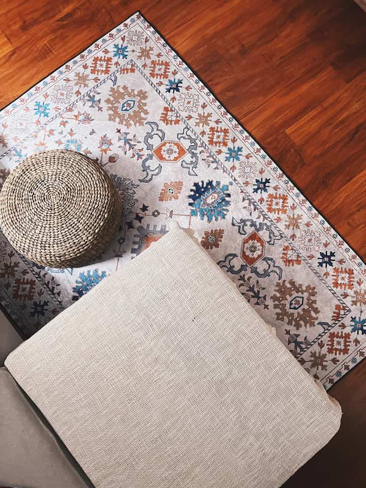 Cozy space with wood tone flooring, Bohemian patterned carpet, and natural material ottoman