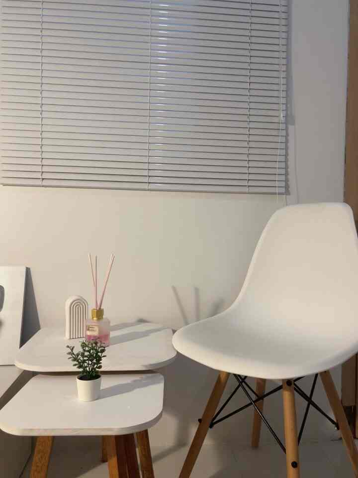 White-toned small room featuring a simple white chair, nested tables, and aluminum blinds creating a clean interior