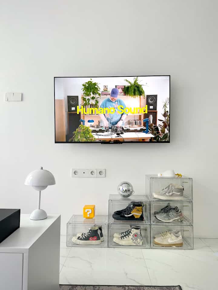White-toned living room featuring transparent shoe boxes and a wall-mounted TV with a minimalist, clean atmosphere