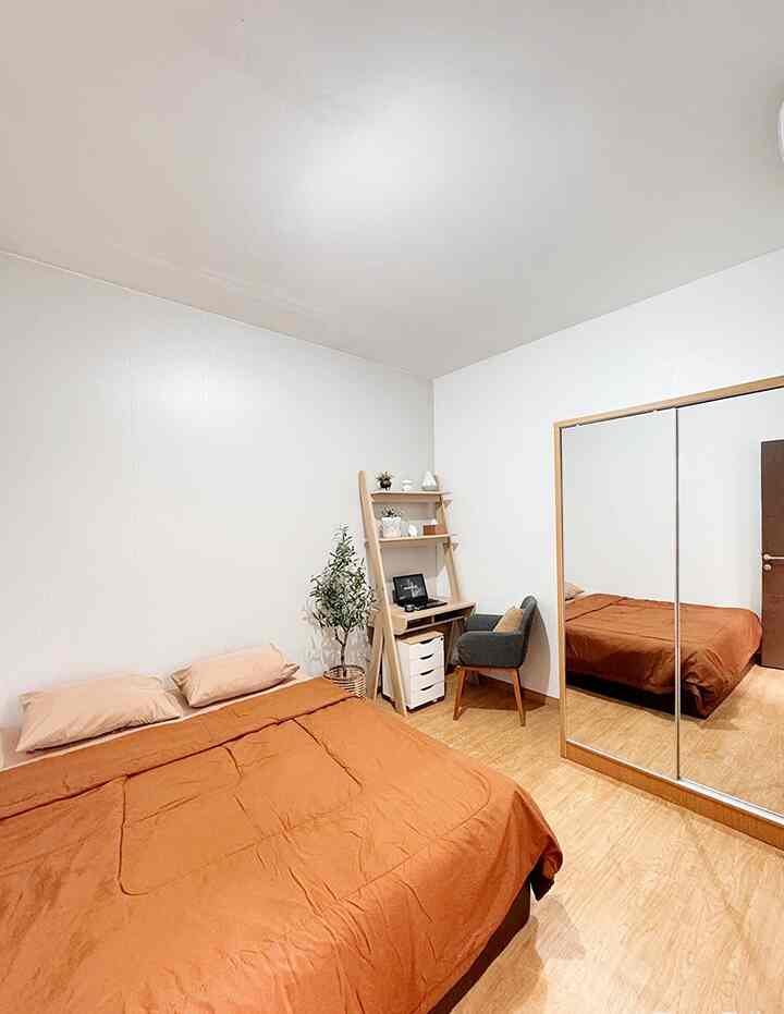 Small bedroom with white walls and ceiling, brown bedding, and wood-tone floor featuring a bed, ladder desk, and gray chair in a natural, minimal style