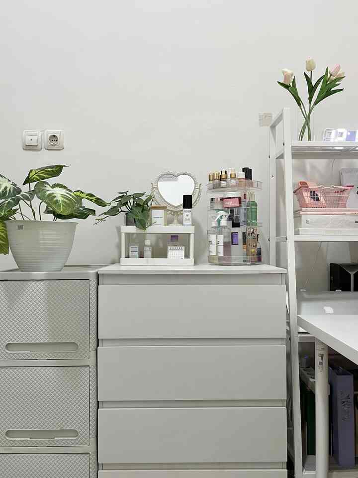 White-toned skincare and makeup corner featuring storage drawers, a heart-shaped mirror, and green plants in a tidy space