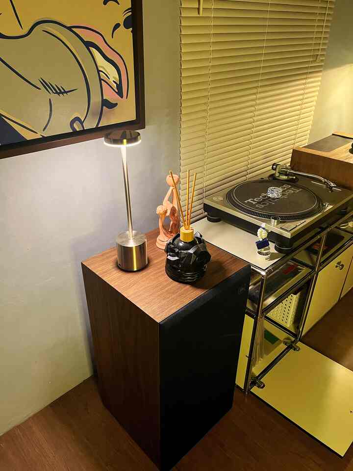 Cozy music listening corner with warm wood tones and soft lighting, featuring a diffuser and table lamp on a side table in a living room setting