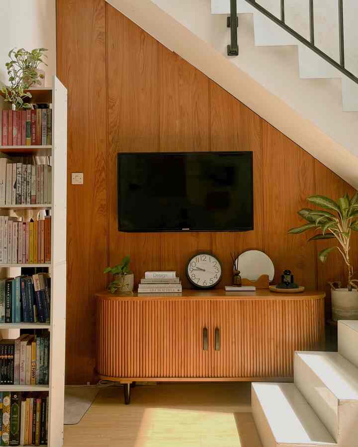 Natural wood-tone corner living space with TV stand and storage under staircase, compact and warm atmosphere